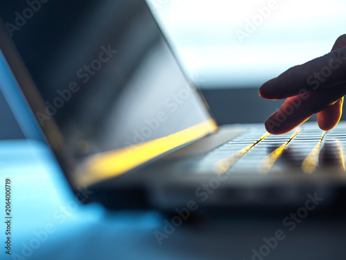 Fingers touch glowing keyboard of a laptop in a dimly lit room.