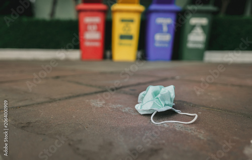Obraz na płótnie Used medical face mask discard on pavement floor on blurred recycle bin or trash