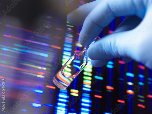 Gloved hand holding vial against colorful DNA sequencing background.
