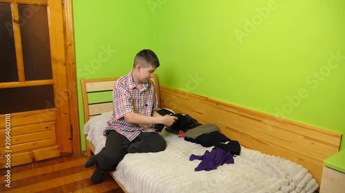 A boy sits on the bed folding clothes, organizing his room and neatly arranging items around him.