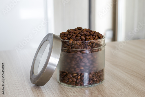 Glass jar filled with aromatic coffee beans rests on wooden surface.