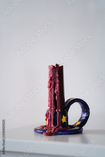 Unlit melted red wax candle in a handmade candle holder. Close everyday still life showing imperfection, craft, and quiet domestic atmosphere.