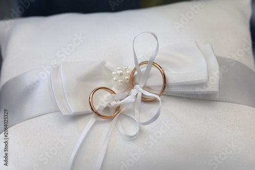 Gold wedding bands tied on white ring pillow