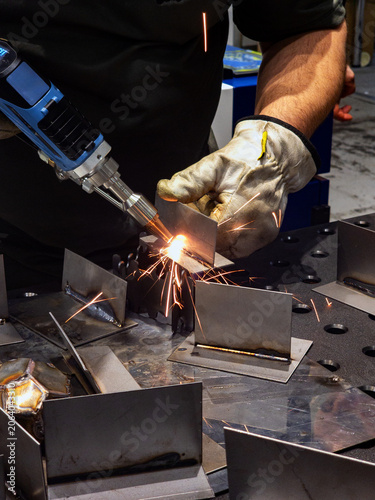 Close-up of Handheld Laser Welding Process on Steel Parts with Bright Sparks in Metalworking Shop