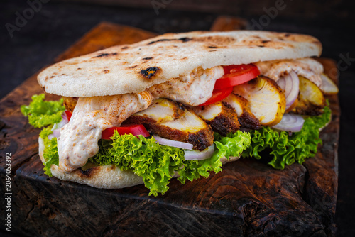 Classic fingerfood fastfood snack -  traditional panino imbottito - Italian flat bread sandwich with roasted chicken, vegetable salad and dressing sauce served as close-up on a wooden board