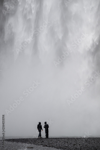 A person walks along Skogafoss waterfall. The mist from the waterfall creates a soft, atmospheric effect. Power and energy Icelandic landscape nature