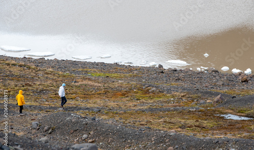 Hikers in protective clothing walking along a glacier fed lake shoreline, observing melting ice floes and the effects of climate change. svinafellsjokull glacier lake Iceland