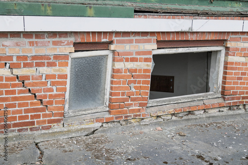 Damaged brick wall with a broken window shows signs of structural issues.