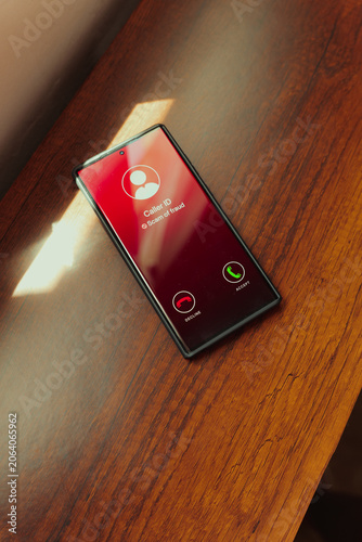 Scam call alert on smartphone screen with red caller ID warning on wooden desk. Scam awareness, fraud prevention, and digital security.