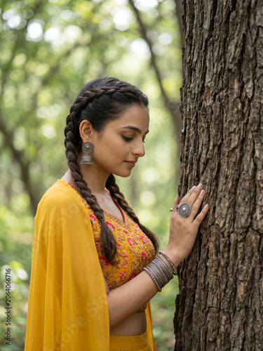 Young Indian Woman Touching Tree Bark In Serene Forest Wearing Yellow Ethnic Fashion Outfit generative ai