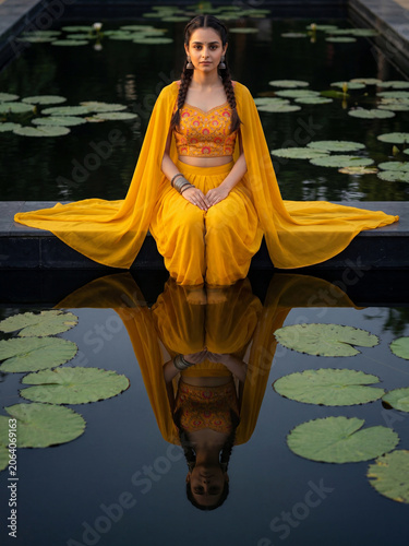 Young Indian Woman In Yellow Ethnic Attire Sitting Beside Lotus Pond With Reflection generative ai