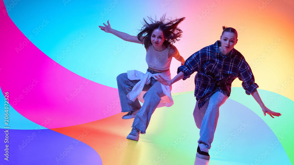 Naklejka premium Two female dancers moving in colorful neon studio with abstract background. Concept of dance crew, youth lifestyle, music promotion, street fashion, and creative advertising.