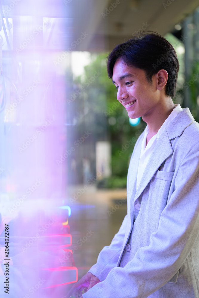 Obraz premium Smiling young nonbinary Thai business professional playing arcade claw machine game