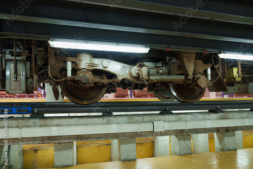 Brightly illuminated train car inspection occurs on concrete subway track within modern industrial station environment, highlighting mechanical maintenance and engineering infrastructure.