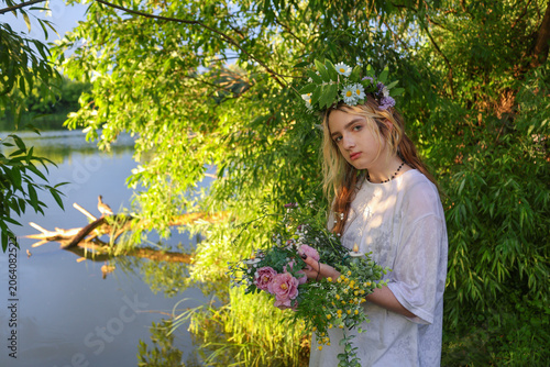 Young ault sitting near the lake water floating floral wreath with candle during Ivan Kupala