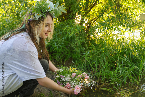 Young ault sitting near the lake water floating floral wreath with candle during Ivan Kupala