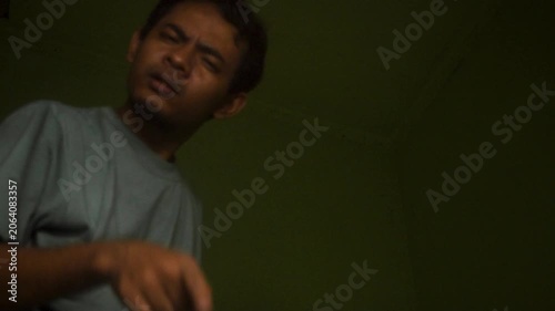 Asian Man In Blue T Shirt Stops And Points Towards Camera In A Dark Dimly Lit Indoor Room Setting