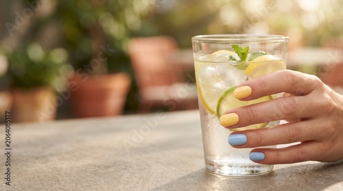 Cuadro en lienzo Hand holding refreshing citrus lemonade with lemon lime mint and ice on outdoor