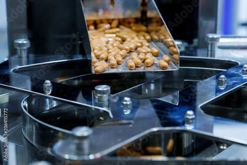 brown medicine capsules or dietary supplements falling from a metal chute into a rotary sorting machine. Pharmaceutical manufacturing and industrial mass production packaging process.