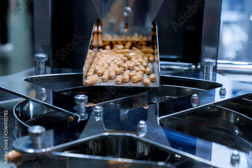 brown medicine capsules or dietary supplements falling from a metal chute into a rotary sorting machine. Pharmaceutical manufacturing and industrial mass production packaging process.