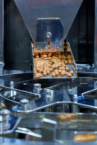 brown medicine capsules or dietary supplements falling from a metal chute into a rotary sorting machine. Pharmaceutical manufacturing and industrial mass production packaging process.