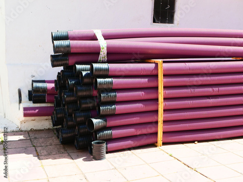 Stack of pink corrugated plastic flexible conduit pipes with black ends at a construction site