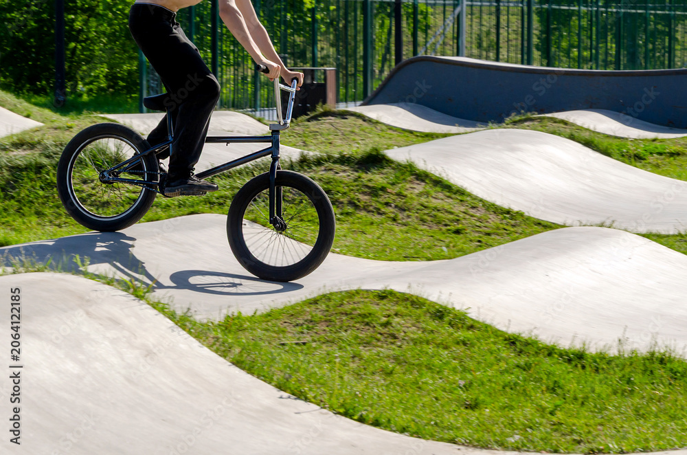 Naklejka premium teen rides bmx bike on concrete pump track with grassy hills. this track provides fun sport and rest for youth. modern track blends eco-friendly design with active outdoor recreation.