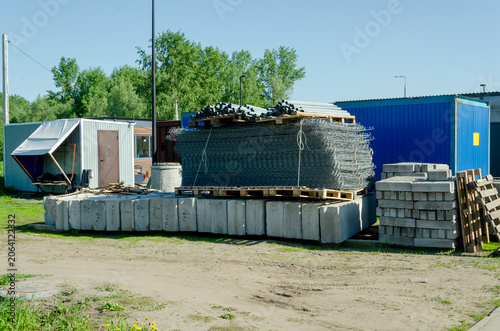 Construction yard with concrete blocks, wire mesh on pallets, storage containers, and building materials on dirt ground. organized materials improve efficiency at modern construction sites