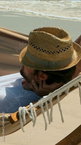 Vertical video: Reclining man in straw hat and white T propping head on beach hammock seeking rest