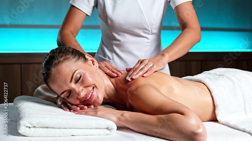 Smiling woman receiving relaxing back massage by professional masseuse in salon. Spa treatment session with oil for body health and wellness, beauty care concept.