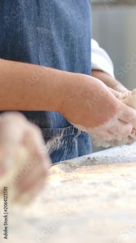 Vertical video: Shaping dough at start, denim-apron baker forming loaf on floured bench for baking