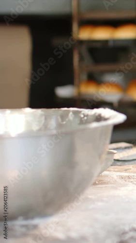 Vertical video: Reaching forearm in white sleeve pulling flour from steel bowl at bakery, for dough