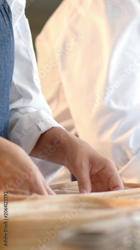 Vertical video: Picking dough baker pinching and folding to proof at bakery, bannetons white coat