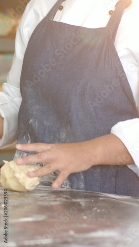 Vertical video: Lifting dough, chef in jacket and apron shaping at bakery counter checking tablet