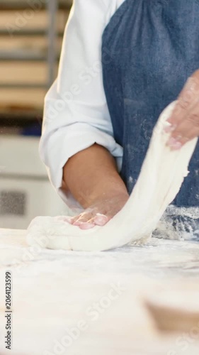 Vertical video: Picking up dough baker in white coat and blue apron shaping at bakery for proofing