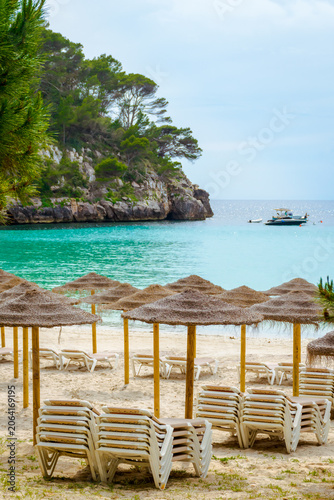 View of famous Cala Galdana beach with empty sun loungers and umbrellas on a sunny day, Menorca Island, Spain