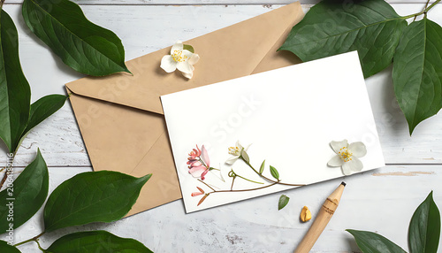 Floral Envelope and Blank Card Surrounded by Green Leaves and Wood Background