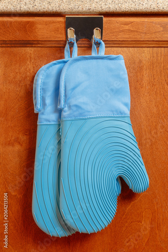 Pair of blue silicone oven mitts hanging from a cabinet door hook in a home kitchen, showcasing heat protection, cooking safety, and kitchen organization.