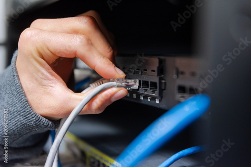 Fotografie Close-up of a technician's hand plugging a grey ethernet network cable into a router or switch port