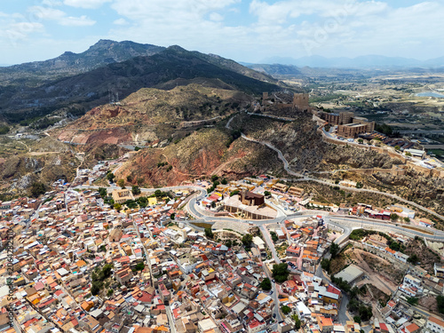 Aerial view of urban cityscape, cloudy sky, mountains, residential buildings of Lorca city with hilltop castle. Murcia, Spain
