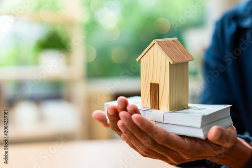 фотографія Real estate investment and property wealth concept featuring a wooden house model on cash savings, home ownership, mortgage financing, financial security, asset growth, and housing investment