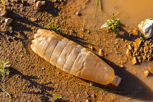 Canvas-taulu Discarded plastic bottle lying in muddy water on a dirt ground, environmental po