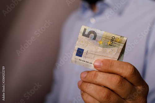 Φωτογραφία A man's hand is holding a five euro banknote, showing the currency symbol and de