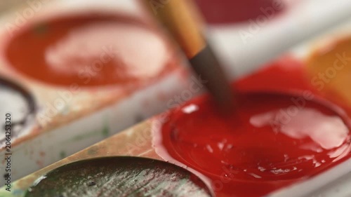 A man dips a brush into red paint for his crative hobby, creative process, and relaxing art therapy session.
