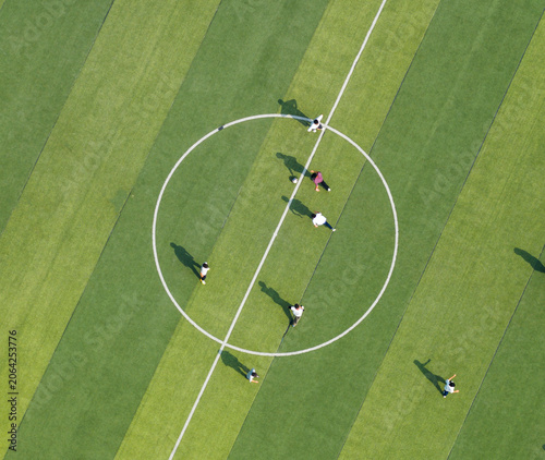 Aerial view of students playing soccer on a green campus field. Promoting physical education and teamwork during break time. Vibrant school sports scene.	
