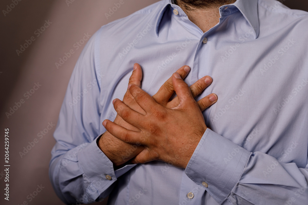 Fototapeta premium Close up of a man in a blue shirt clutching his chest in distress.