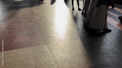 Close-up of traditionally dressed Indian people walking across a sunlit floor, with moving feet and sharp shadows creating dynamic patterns during a cultural gathering or festival