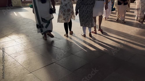 Close-up of traditionally dressed Indian people walking across a sunlit floor, with moving feet and sharp shadows creating dynamic patterns during a cultural gathering or festival