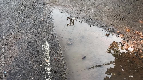 Reflections of electric poles, power lines, and trees shimmering in rainwater collected in a roadside pothole, creating an abstract urban landscape after rainfall
