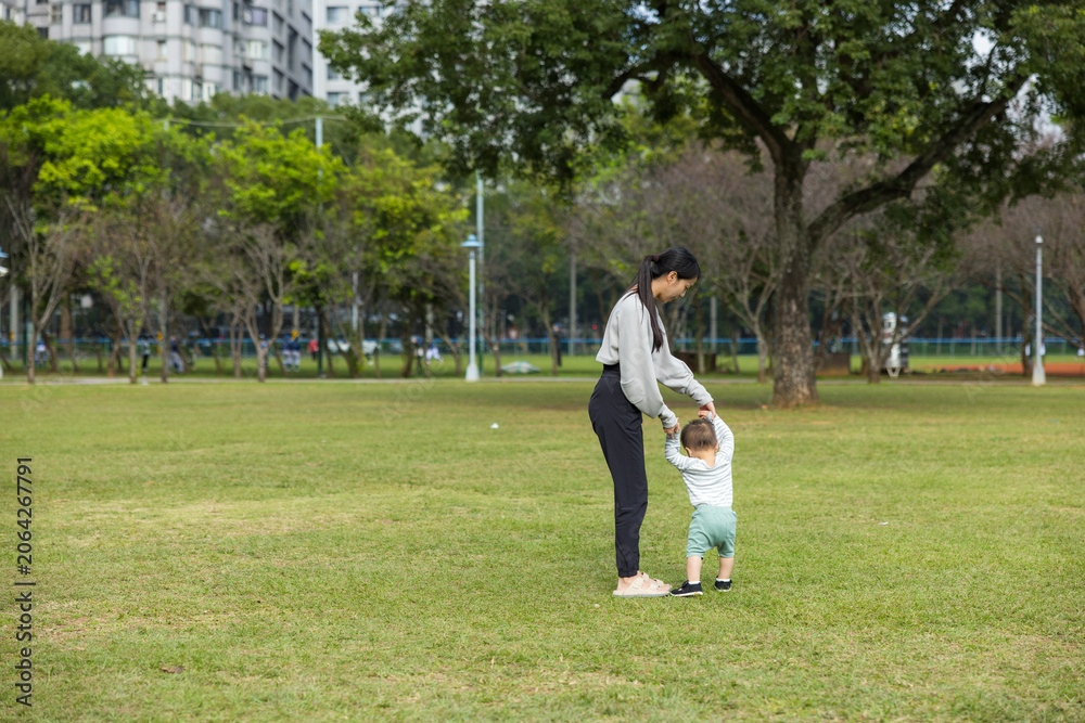 Fototapeta premium Mother watching her little toddler walk on grass